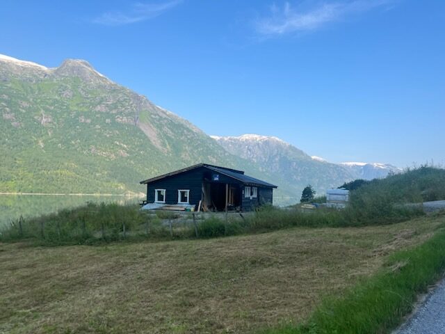 Bygningen ved plassen sett frå vegen, med vatnet og fjell bak
